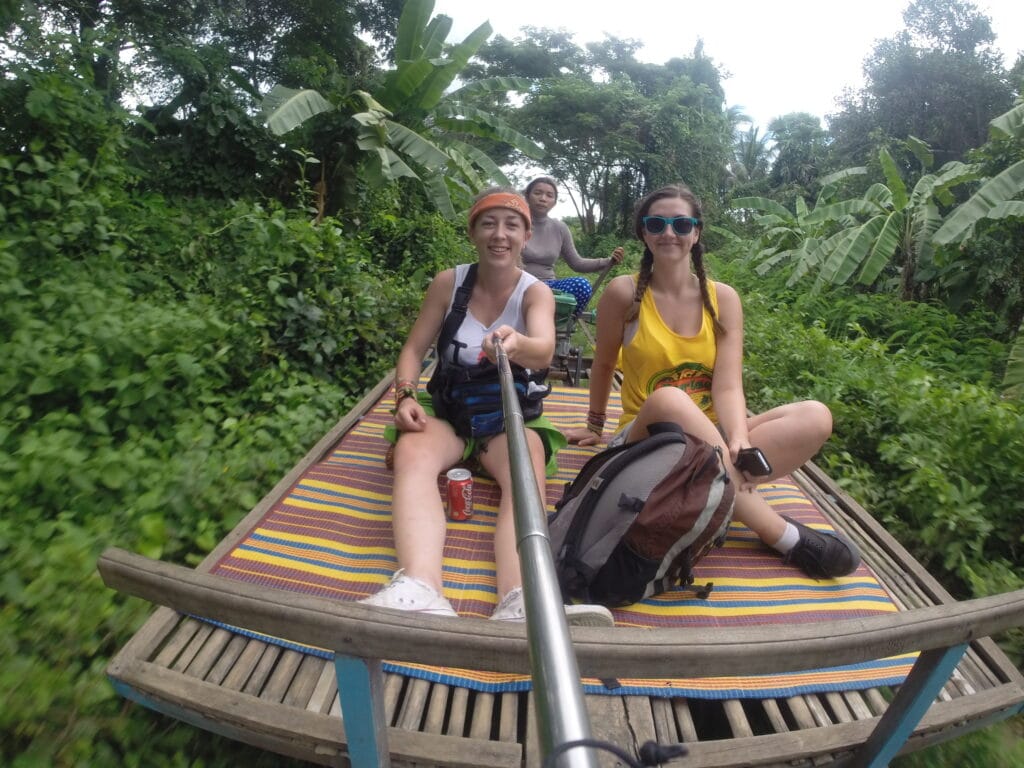 2 people on a bamboo train riding rhough the cambodian town battambang